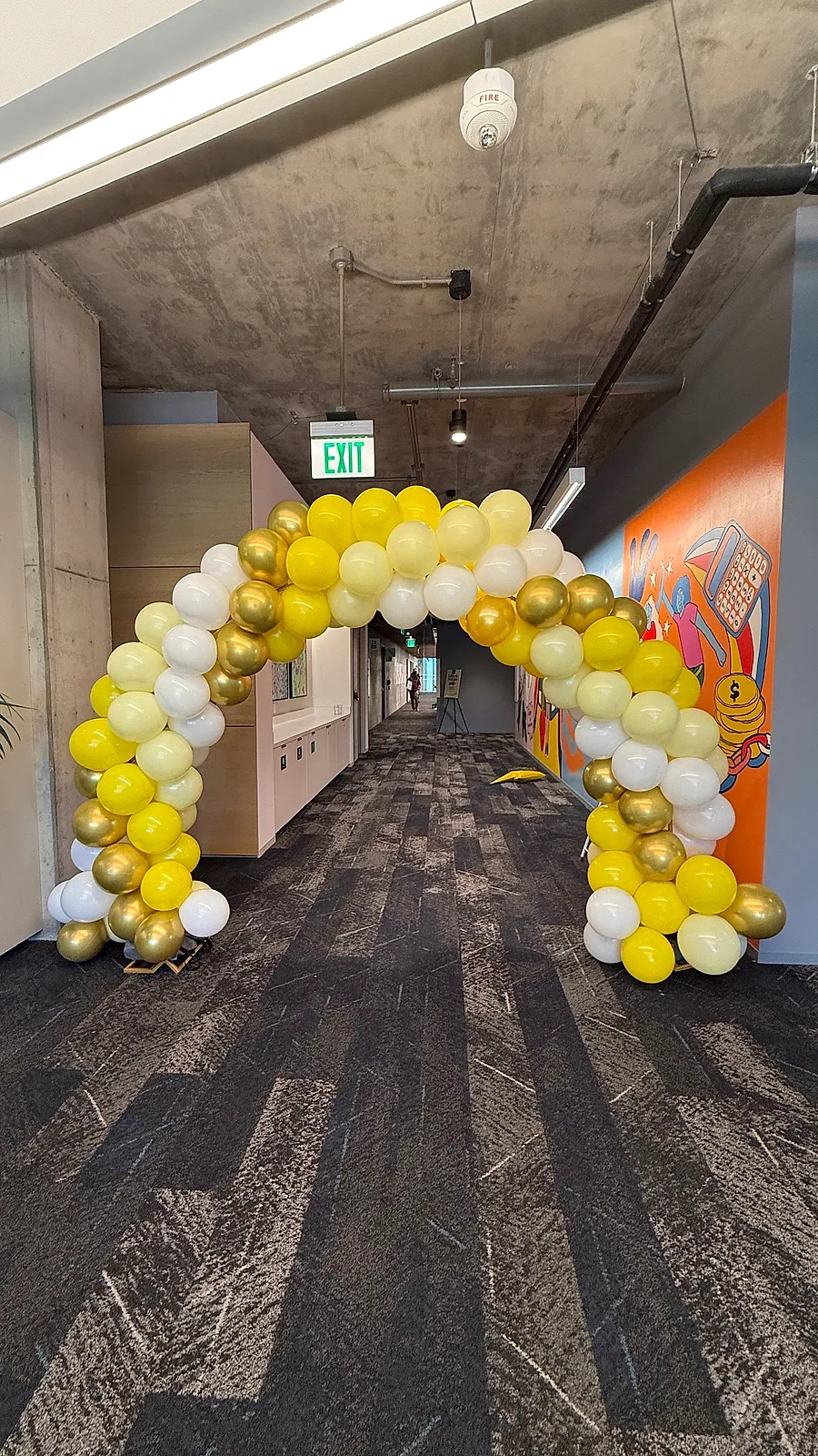 Yellow, gold and white organic balloon arch spanning an office corridor, built floor to floor so people walk through it
