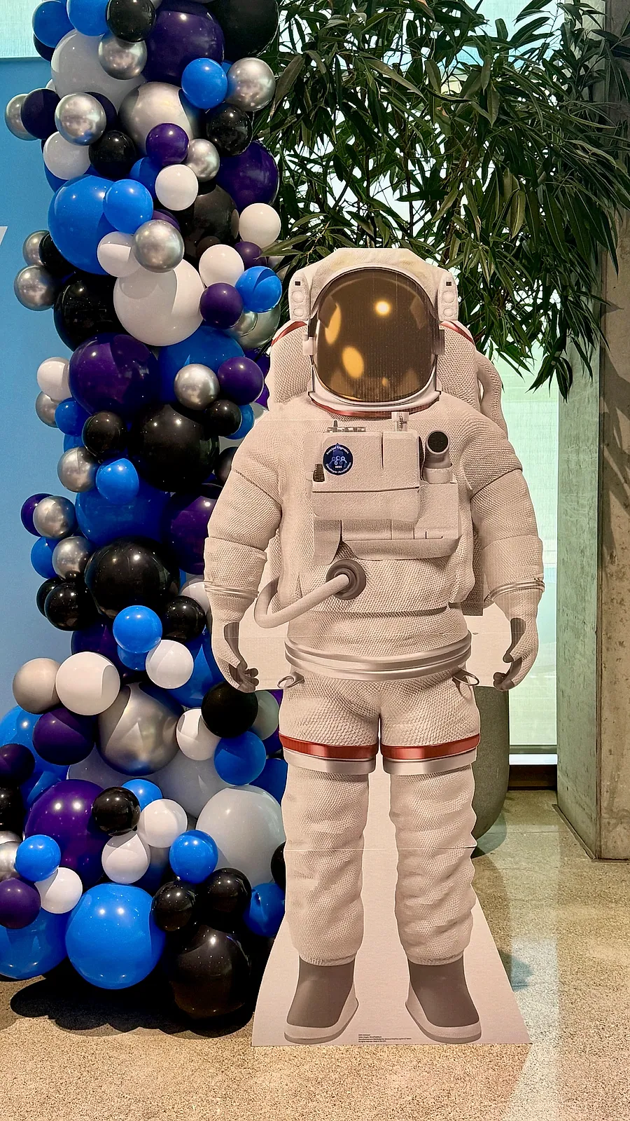 Purple, black, silver and blue balloon column beside a life-size astronaut cutout used as a photo backdrop