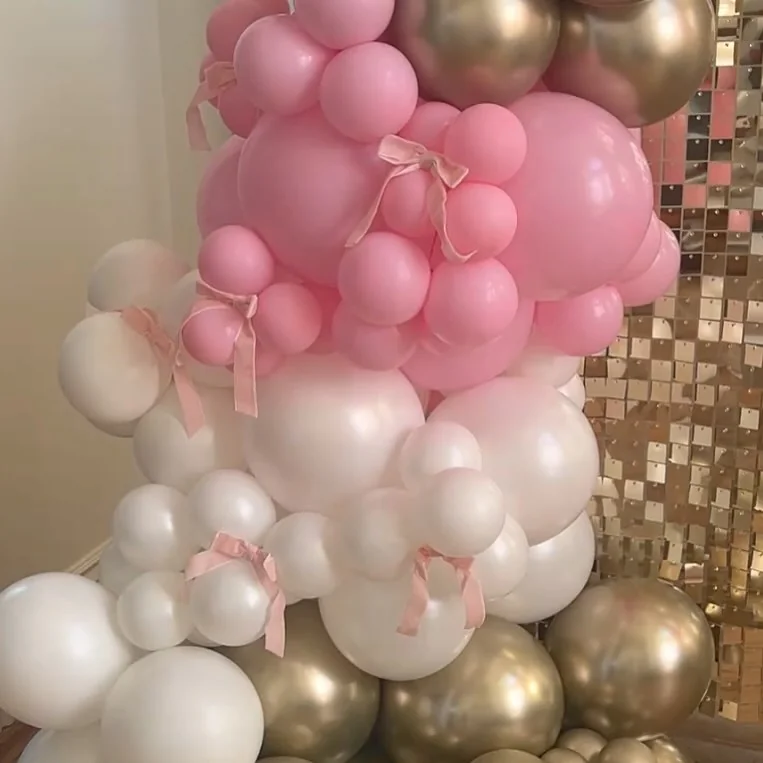 Pink, white and gold chrome balloon garland with pink ribbon bows in front of a gold sequin wall