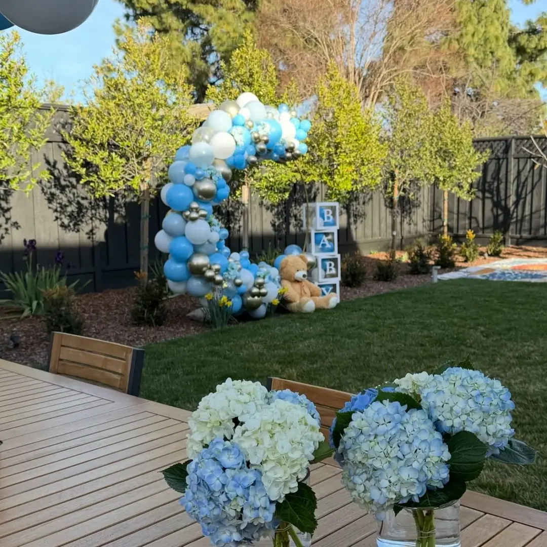 Outdoor balloon garland installation in a backyard setting with greenery