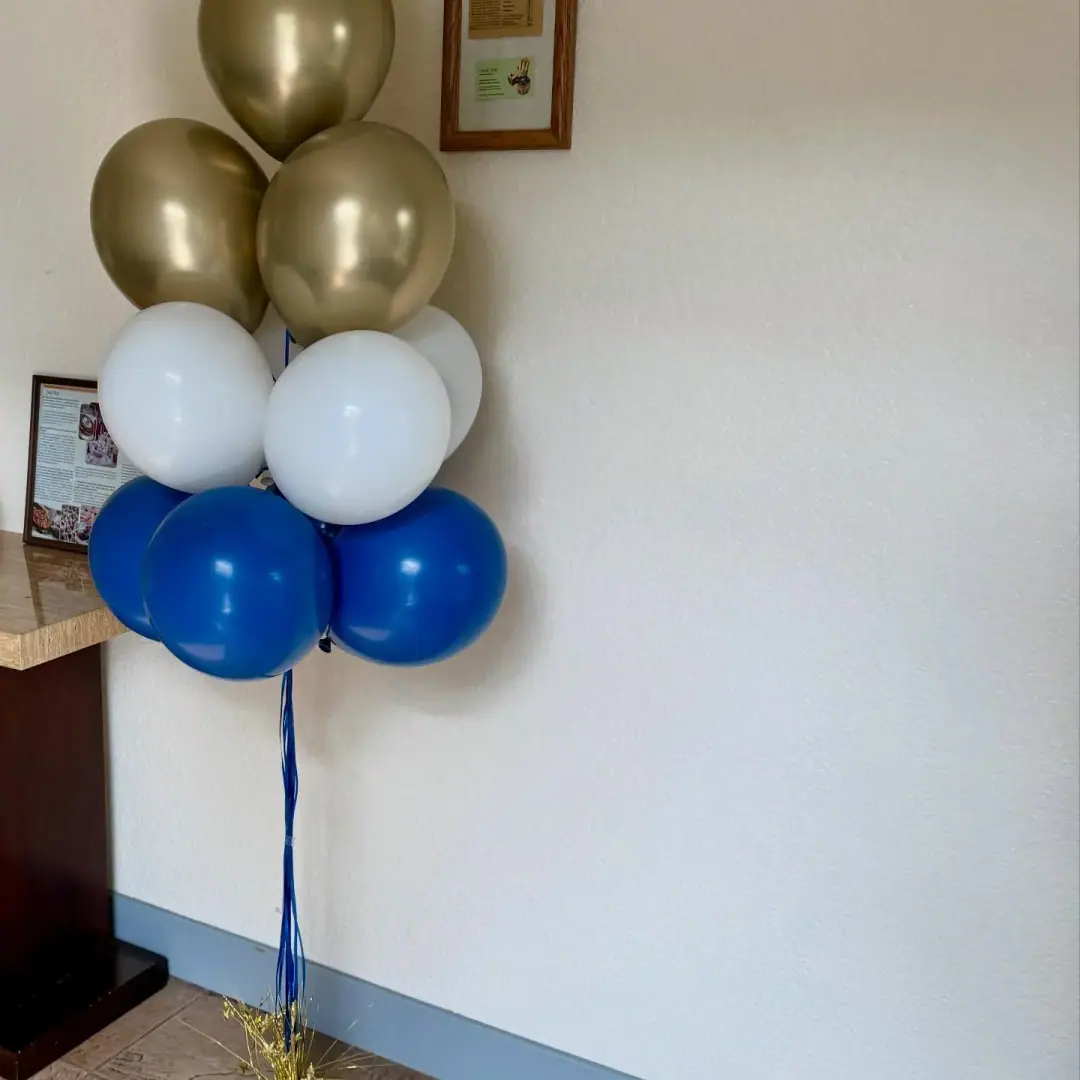 Helium balloon bouquet in chrome gold, white and royal blue, weighted beside a counter against a white wall