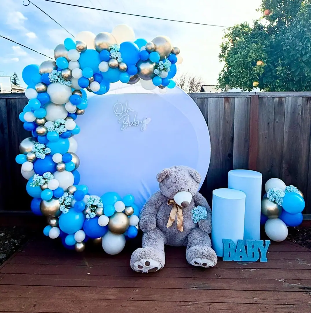Blue, white and gold chrome organic balloon garland around a round backdrop on an outdoor backyard deck in daylight