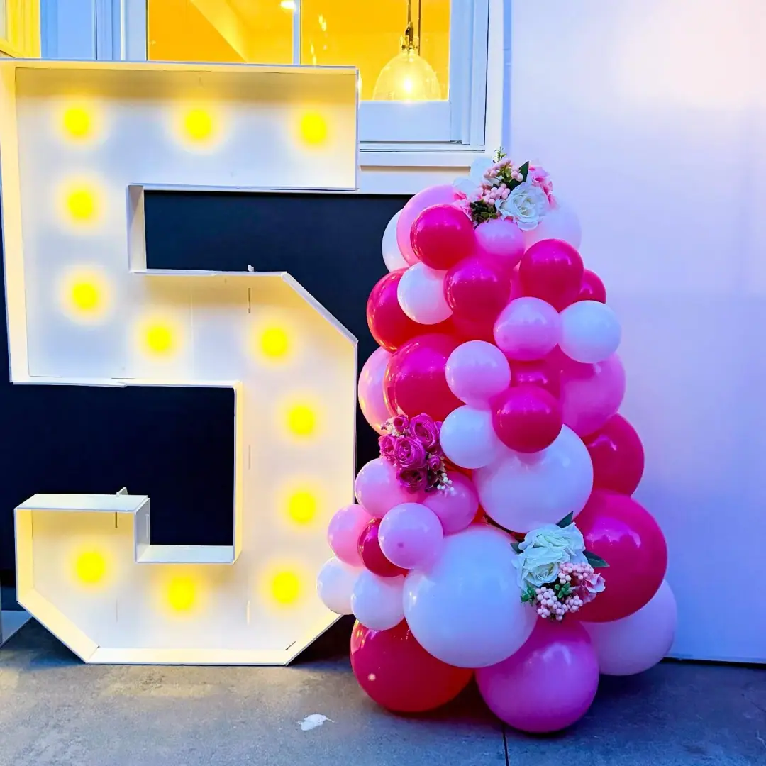 Light-up marquee number beside a pink, white and red balloon column with flowers at a 15th birthday
