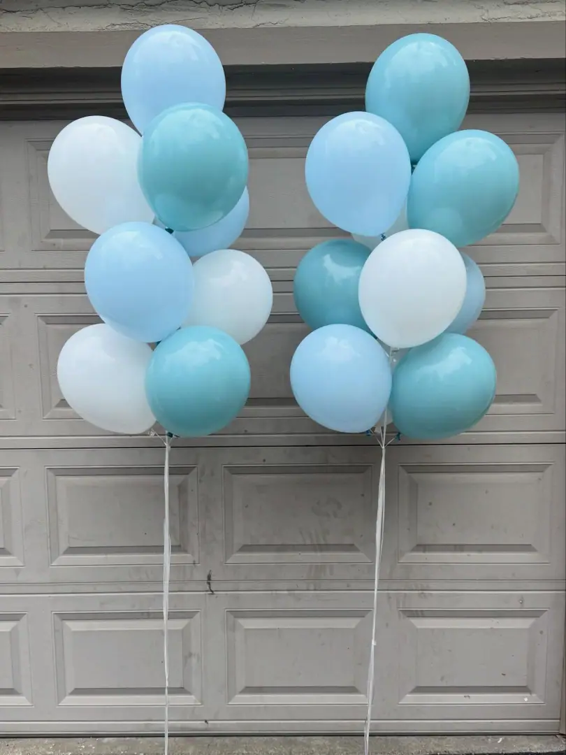 Two pale blue, aqua and white latex balloon bouquets on white ribbons in front of a garage door
