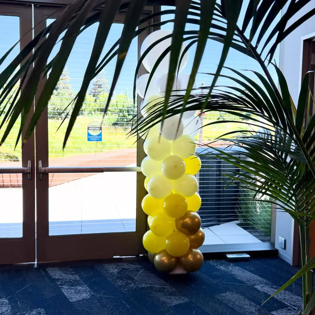Air-filled balloon column in white, yellow and gold standing beside glass doors at an office entrance