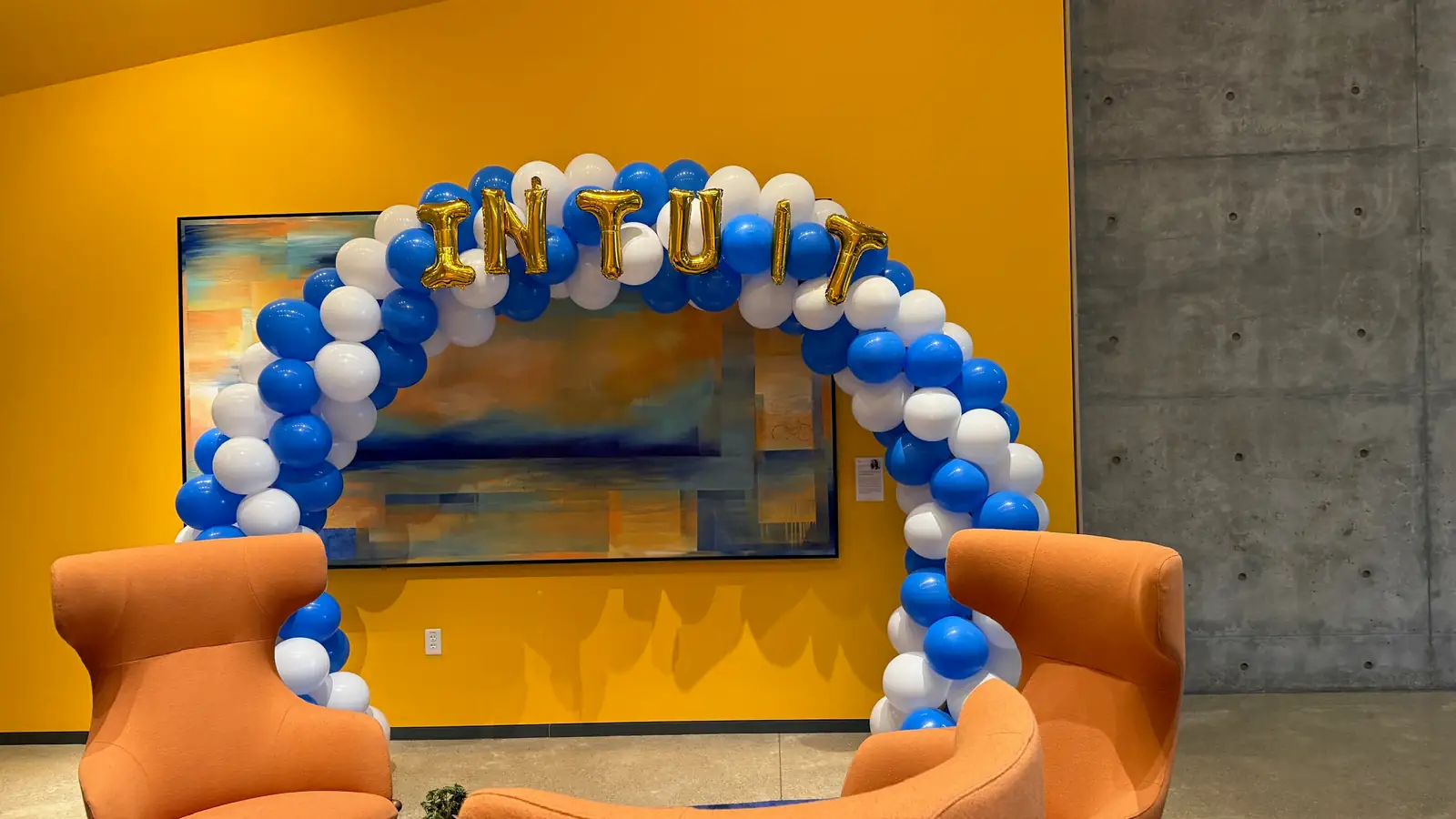 Blue and white balloon arch topped with gold INTUIT letter balloons over an office lounge
